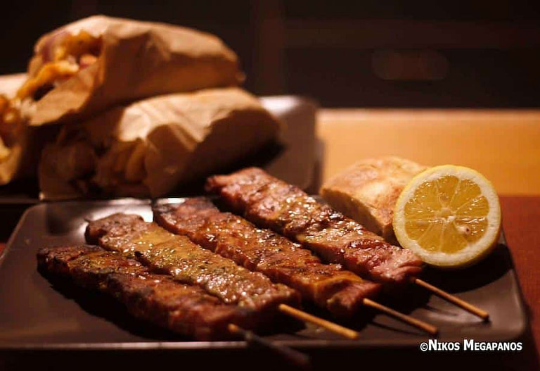 close-up of wooden sticks with cooked Greek souvlaki on plate and a half of lemon