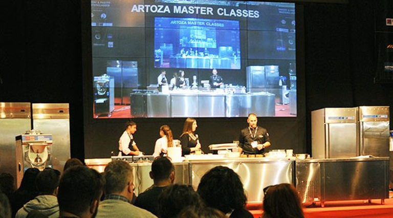 people on the table and screen that says ‘Αrtoza Masterclasses’ in the background