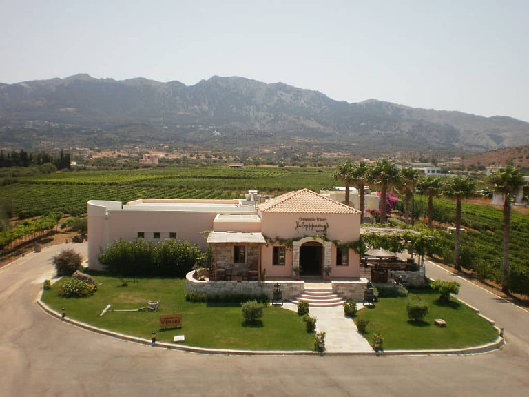 Hatziemmanouil Winery from above surrounded by vineyards, palm trees, lawn grass and mountains