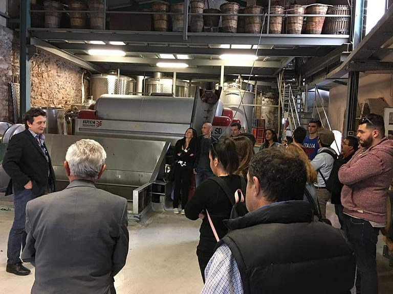 guide presenting tourists the 'Nikolou Winery' plant in front of grape press machine