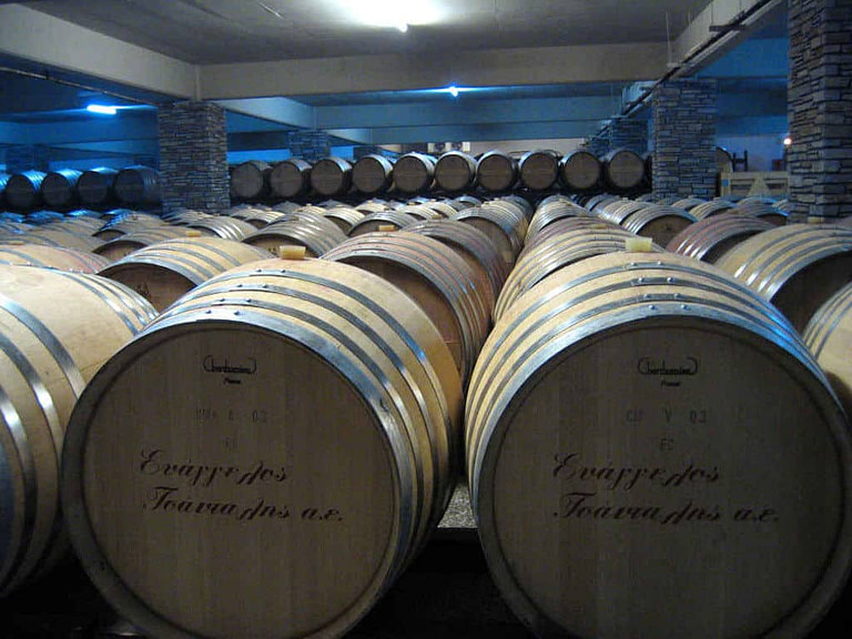 lying personalized wooden wine barrels sign with the 'Tsantali Winery' logo in a row in the stone cellar