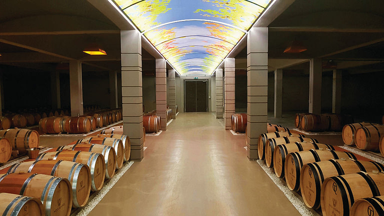 lying wine wooden barrels in a row at 'Nico Lazaridi' cellar that has painted ceiling