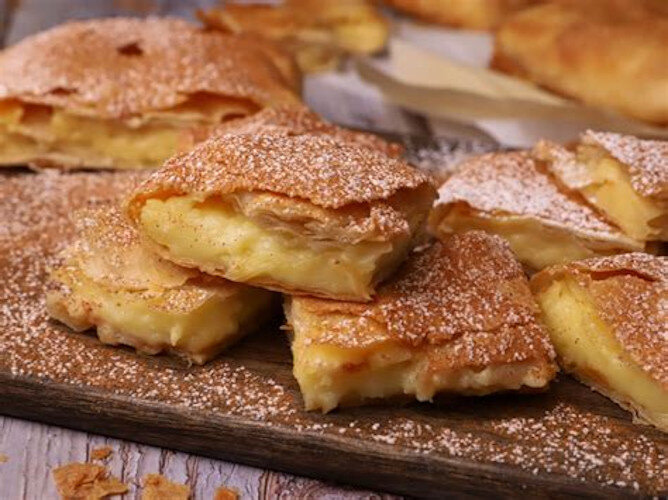 Close-up of pieces of ‘Bougatsa’ means filo dough with white cream on wood surface and one of the piece is on top of others