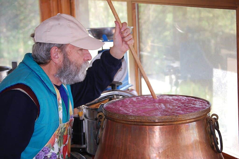 man mixing with a wooden rod in a bronze cauldron, the must 'pulp' of black grapes boiling at 'Vaimakis Family' facilities