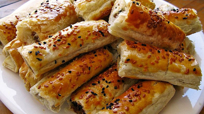 Close-up of pieces on top of each others of ‘Boureki’ as a pita baked in a large pan with sesame seeds and then cut into smaller serving portions