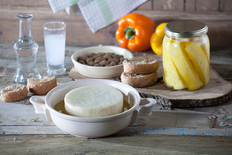 bowl and jar with 'Mystakelli Dairy' white cheeses in oil and pieces of dry bread and bowl with olives on wood surface