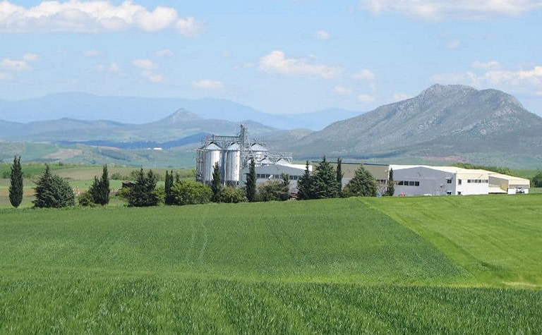 far view of Antonopoulos Farm plant surrounded by green crops and mountains in the background