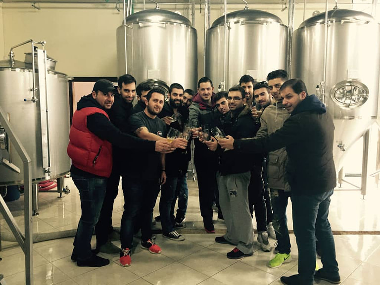 a group of men clink glasses for 'cheers' and smiling happily at the camera at 'Siris Microbrewery' plant