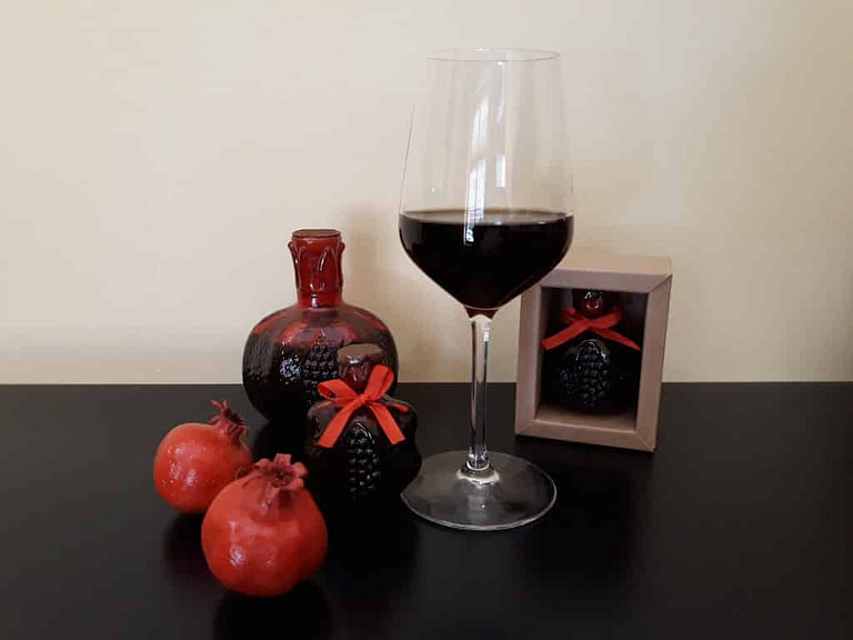glass of red wine and two bottles and ceramic pomegranates at 'Quality Fruit Wines'