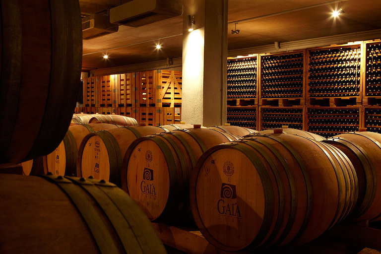 wooden barrels in a row and stacked bottles on top of each other in the storage lockers at illuminated Gaia Wines Nemea cellar