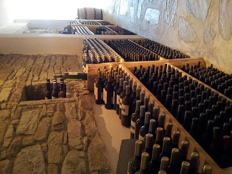 wine bottles on wooden shelves under stone wall at 'Afianes winery' cellar