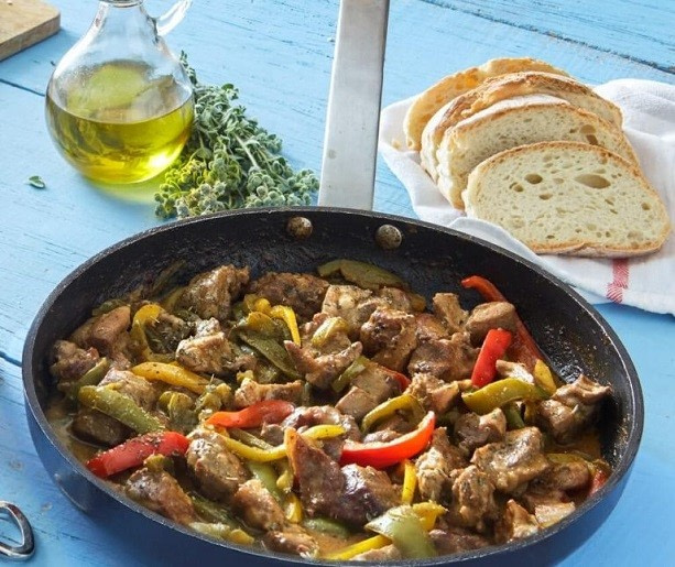 Pan with Greek ‘Tigania’, pieces of meat, and fried in a oil with pepper and herbs, and slices of white bread in the background