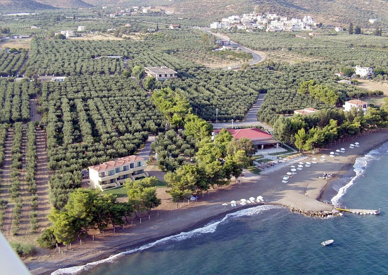 view from above of 'Makis Inn Resort' complex buildings with beach and sea in the front and trees in the background