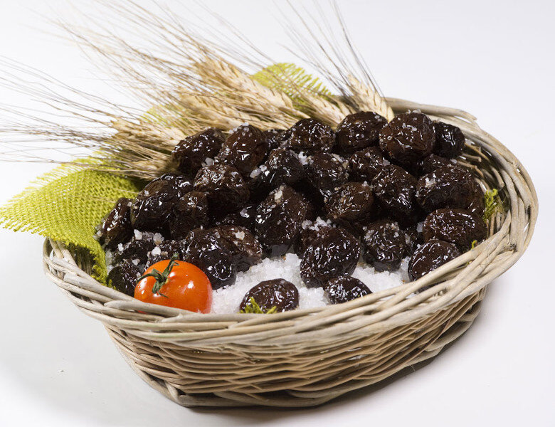 wicker basket with ‘Throumba’ olives are wrinkled, edible black olives and dry wheat ears in the background