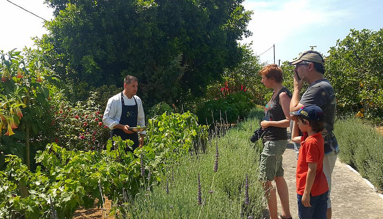 A man giving a guide and a family tourists take photos at En Kefallinia Organic Farm Restaurant garden