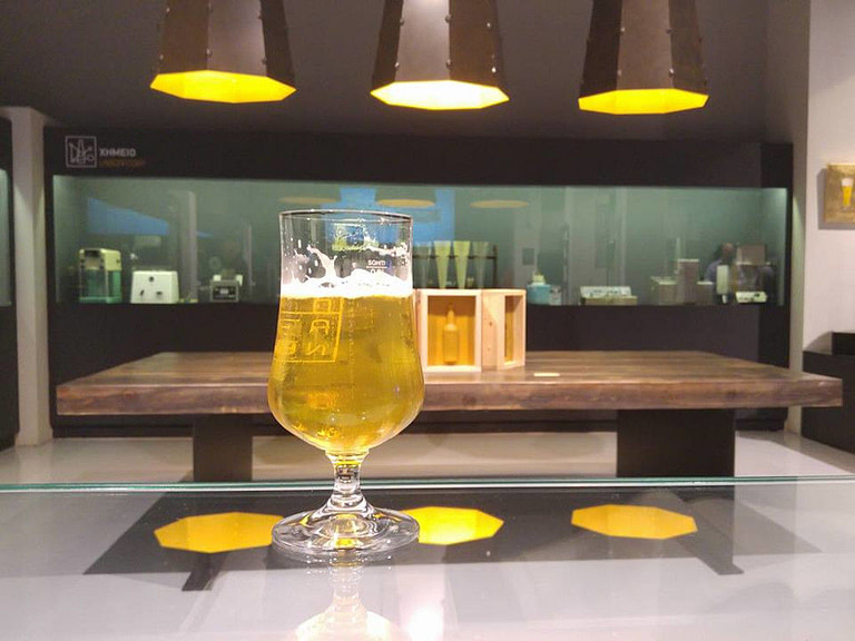 Glass with beer in the background of window with exhibits at 'Athineo Center of Creative Brewing' museum