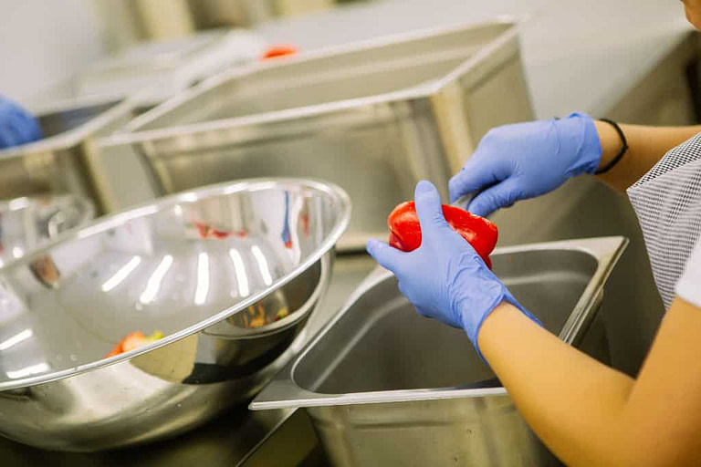 a woman wearing plastic gloves cutting a red 'Florina' pepper with a knife on the aluminum buscket at 'Rizes' plant