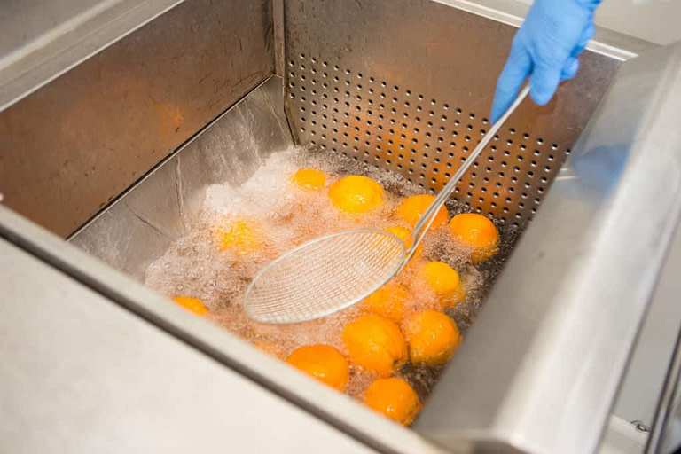 woman with a sieve spoon removing oranges from their washing system